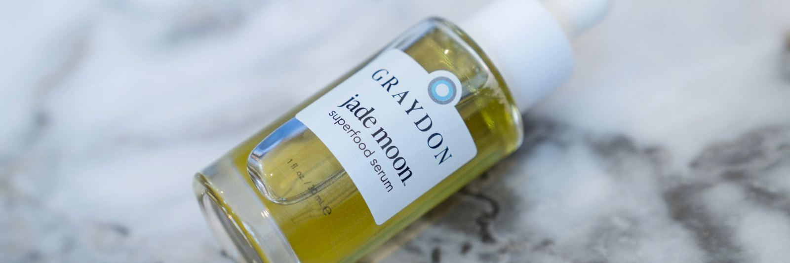 a photo of a full green-yellow bottle of jade moon serum on a marble backdrop
