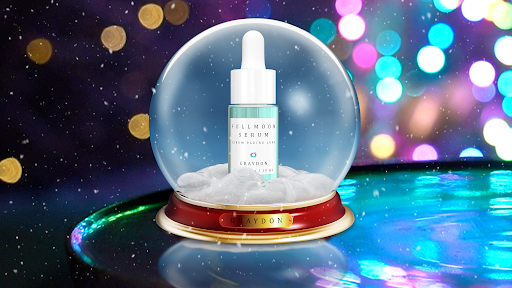 A glass bottle containing an aquamarine-coloured facial serum in a snowglobe with multicoloured lights in the background. 